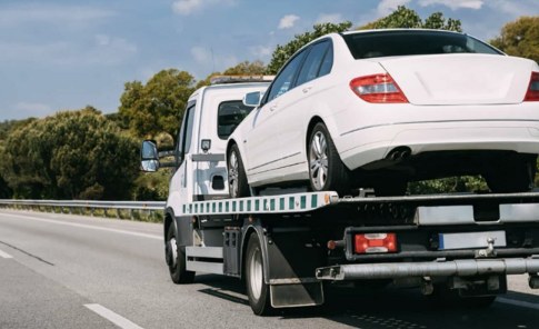 A white car being towed on a flatbed truck on a highway