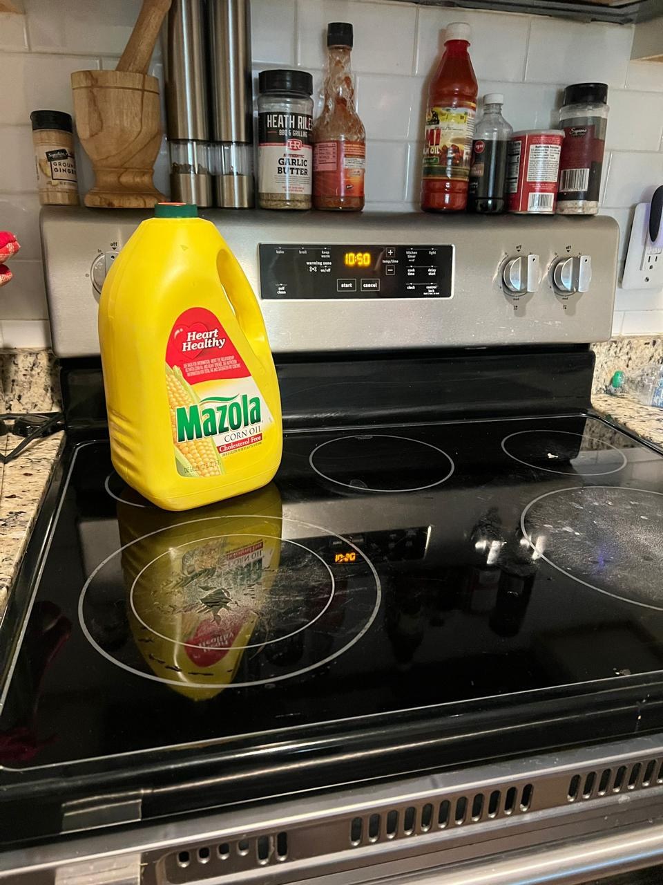 A kitchen stove with a bottle of corn oil and spice containers on the back ledge