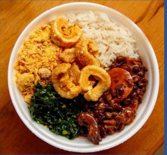 A bowl of rice, beans, collard greens, farofa and pork rinds on a wooden table