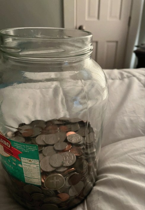 A glass jar filled with coins sitting on a bed